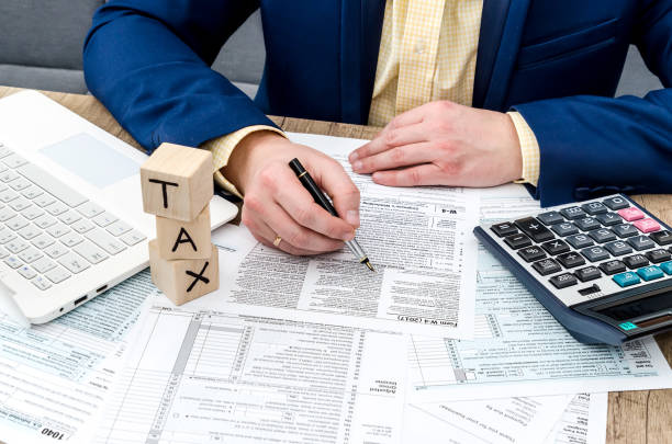 Businessman filling W-4 form with pen, calculator and pc
